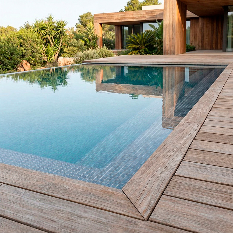 Primer plano de una piscina moderna con borde de madera tecnológica y reflejos de vegetación.